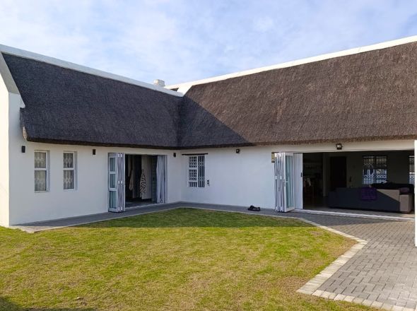 Projects L-shaped residential home layout with a high-density thatched roof overlooking an inner grass courtyard with folding glass doors