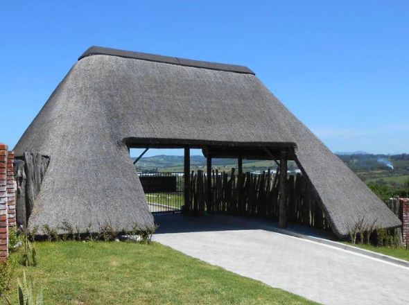 Projects A premium estate entrance gatehouse featuring a distinctively angled, heavy timber frame structure and an expansive high-density thatched roof canopy