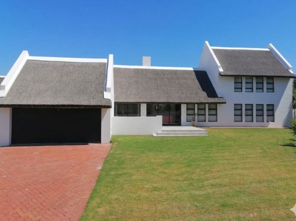 Projects Modern white double-story coastal home featuring a precision straight-line thatch roof and paved brick driveway
