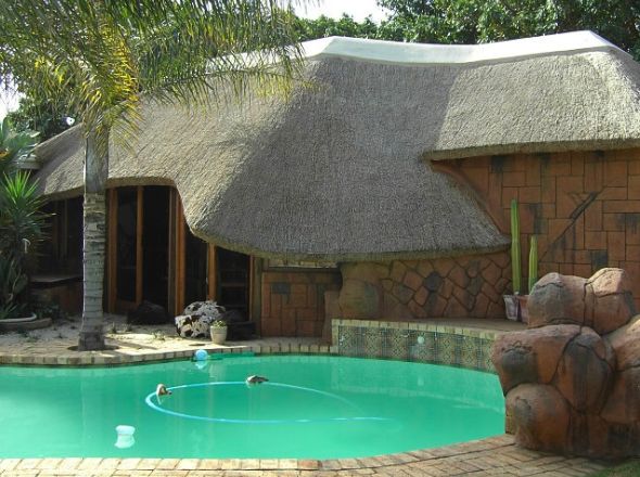 Tropical themed poolside entertainment structure featuring an undulating thatch roof overhang and natural rock textures